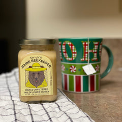 A jar of Swan's Maine Beekeeper Raw & Unfiltered honey next to a hot cup of tea. 