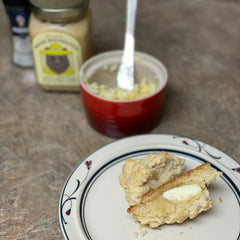A homemade biscuit topped with honey butter sits on a plate next to kitchen ingredients. 