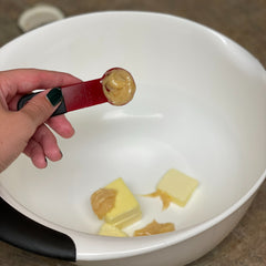 A tablespoon of honey is added into a mixing bowl containing butter. 
