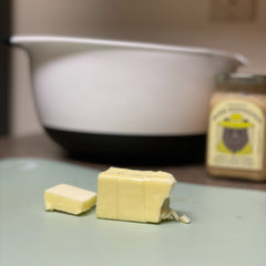 Butter sits on a cutting board in front of a mixing bowl and jar of honey. 