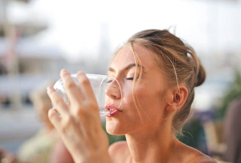 A woman drinking water out of a rounded glass