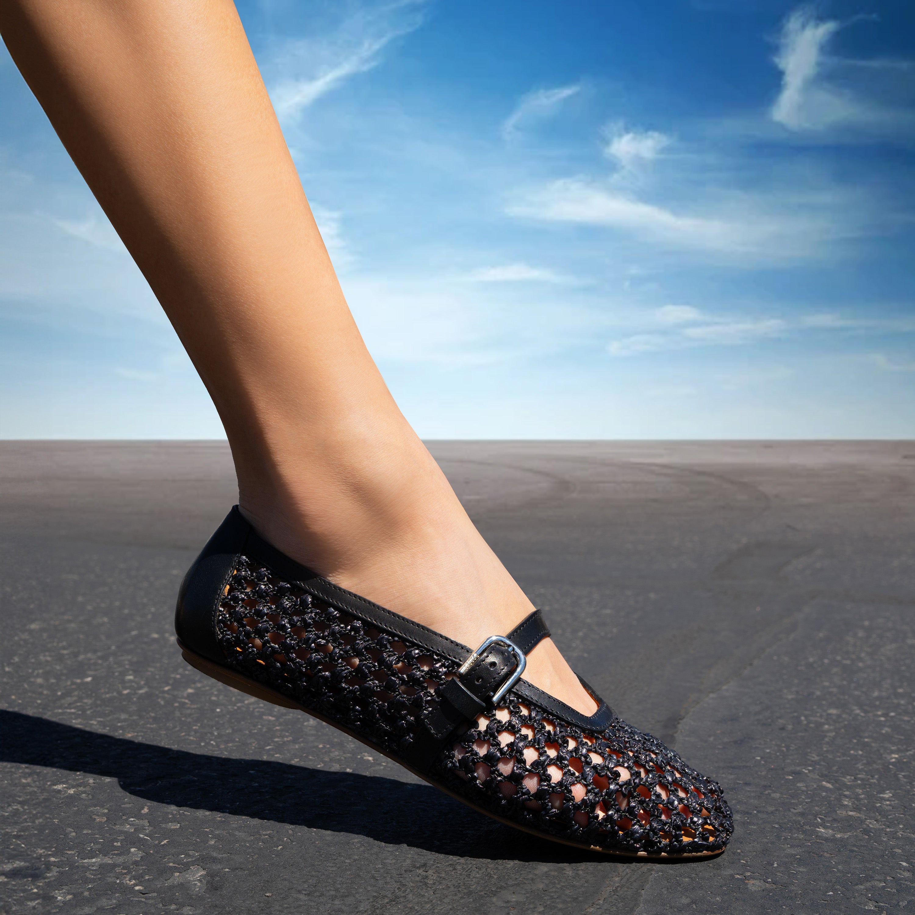 A woman's leg wearing a sparkling black flat shoe on a desert road.