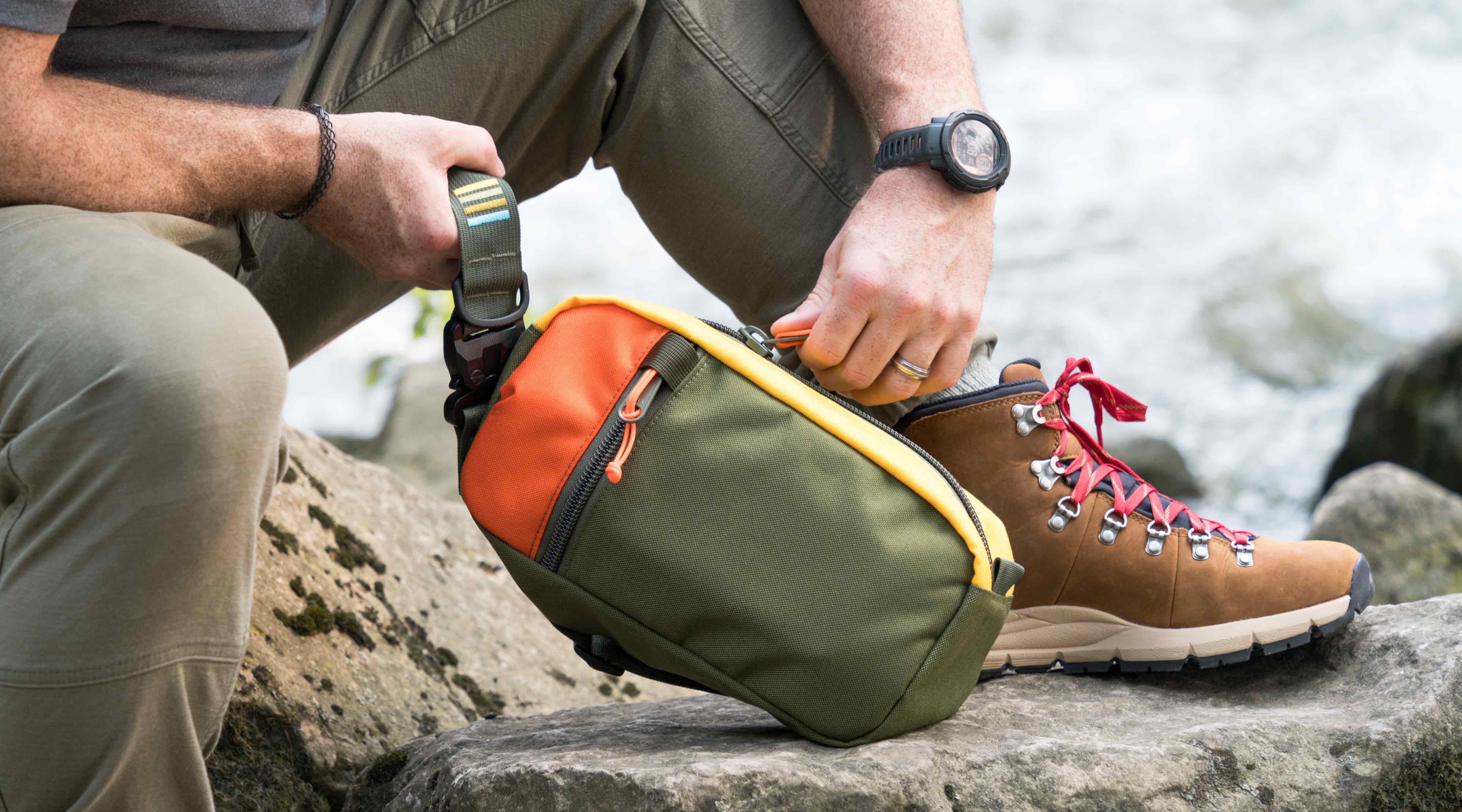 Hayden sling bag used for hiking and outdoor activities.  Shown in olive green and orange.