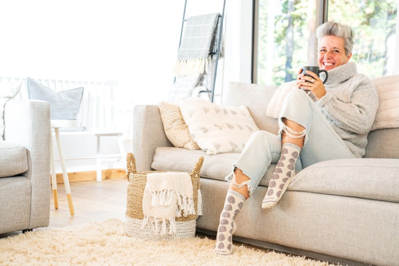 Woman enjoying a cup of coffee on her couch looking comfortable in Sockwell socks