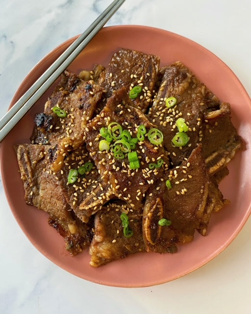 Korean rib aka Galbi by @_dareats plated with sesame seeds and green onion on a plate.