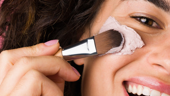 girl applying pink clay mask to her face with a brush