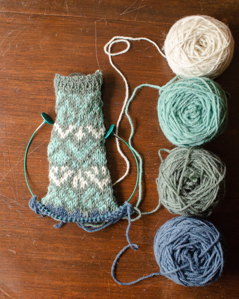 Four balls of yarn in blues and greens, and a slightly messy knitted yoke swatch