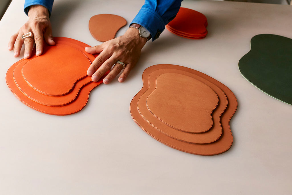 Leather mat pieces in orange and brown on a table, with hands reaching for them