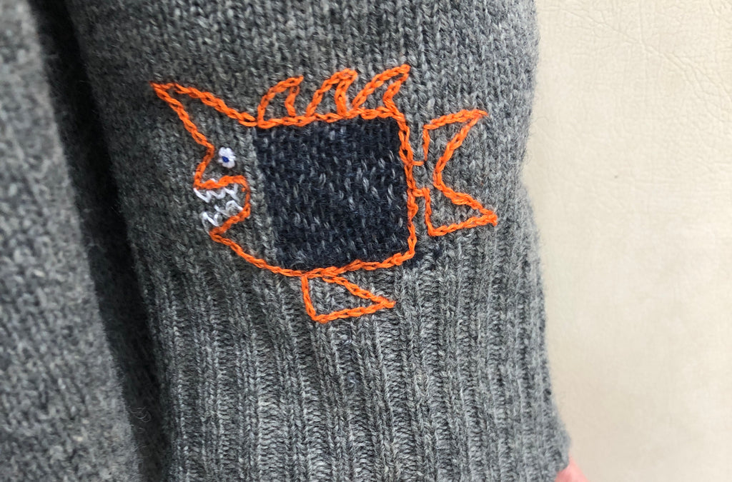 A spiky, cartoony fish darned on a sweater arm.
