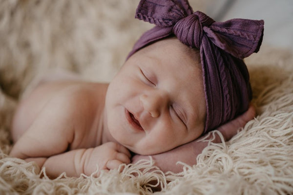 A newborn baby sleeping on a soft blanket with a purple headband on