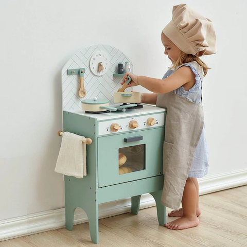 toddler girl playing with small green play kitchen