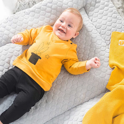 baby wearing yellow top and black trousers laughing