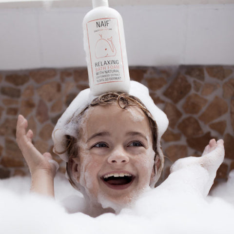 Boy laughing in bubble bath with bottle of bath foam on head