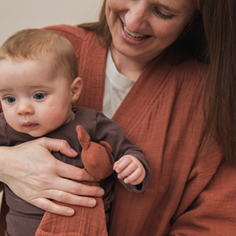 Mum holding baby with rust coloured comforter in hand