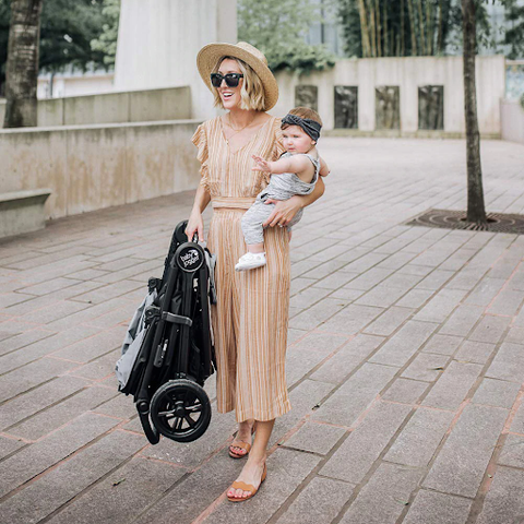 Mum holding folded stroller in one hand and baby in other arm