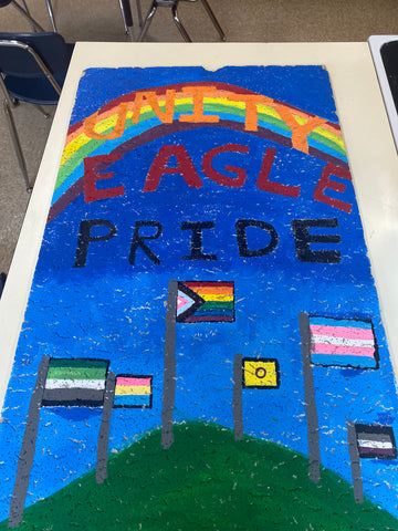 Ceiling tile painted with the words "UNITE EAGLE PRIDE", a rainbow, and a variety of LGBTQ+ community flags