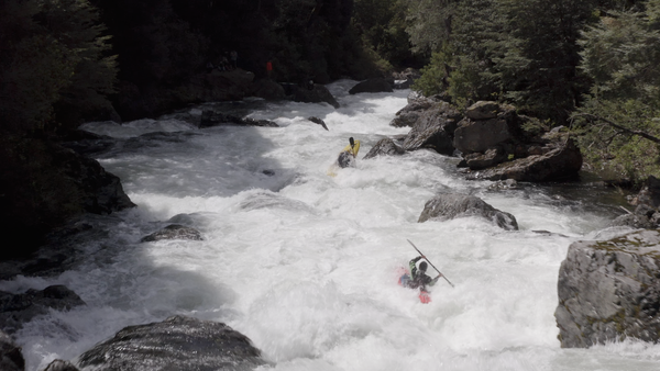 Two whitewater kayakers paddling down a river in Chile.