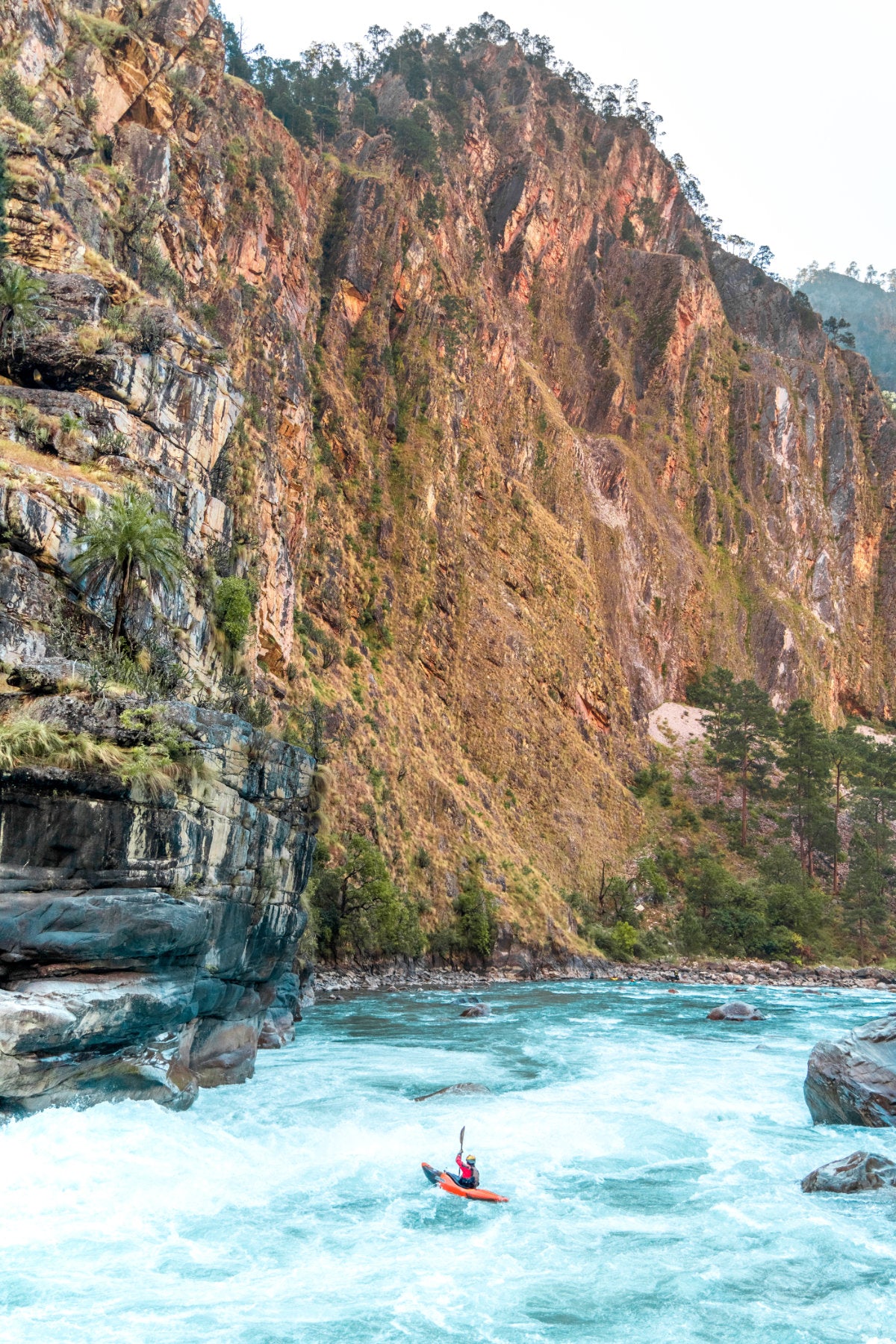 Kayaker paddling in the middle of a whitewater river with large cliff walls on both sides