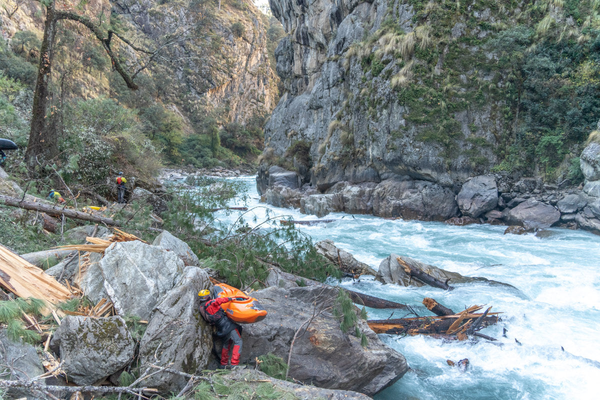 Kayaker lifting kayak onto rocks next to river to portage around a large rapid