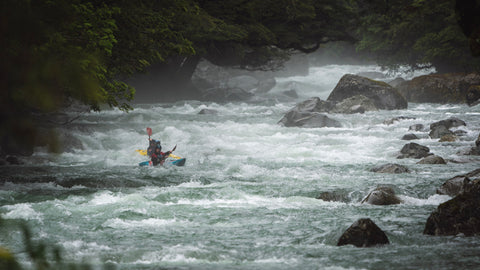 Two kayakers paddling down a remote river in New Zealand.