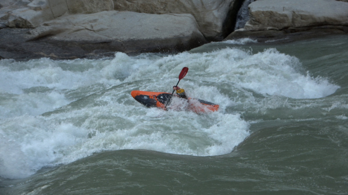 Whitewater kayaker paddling through a river wave