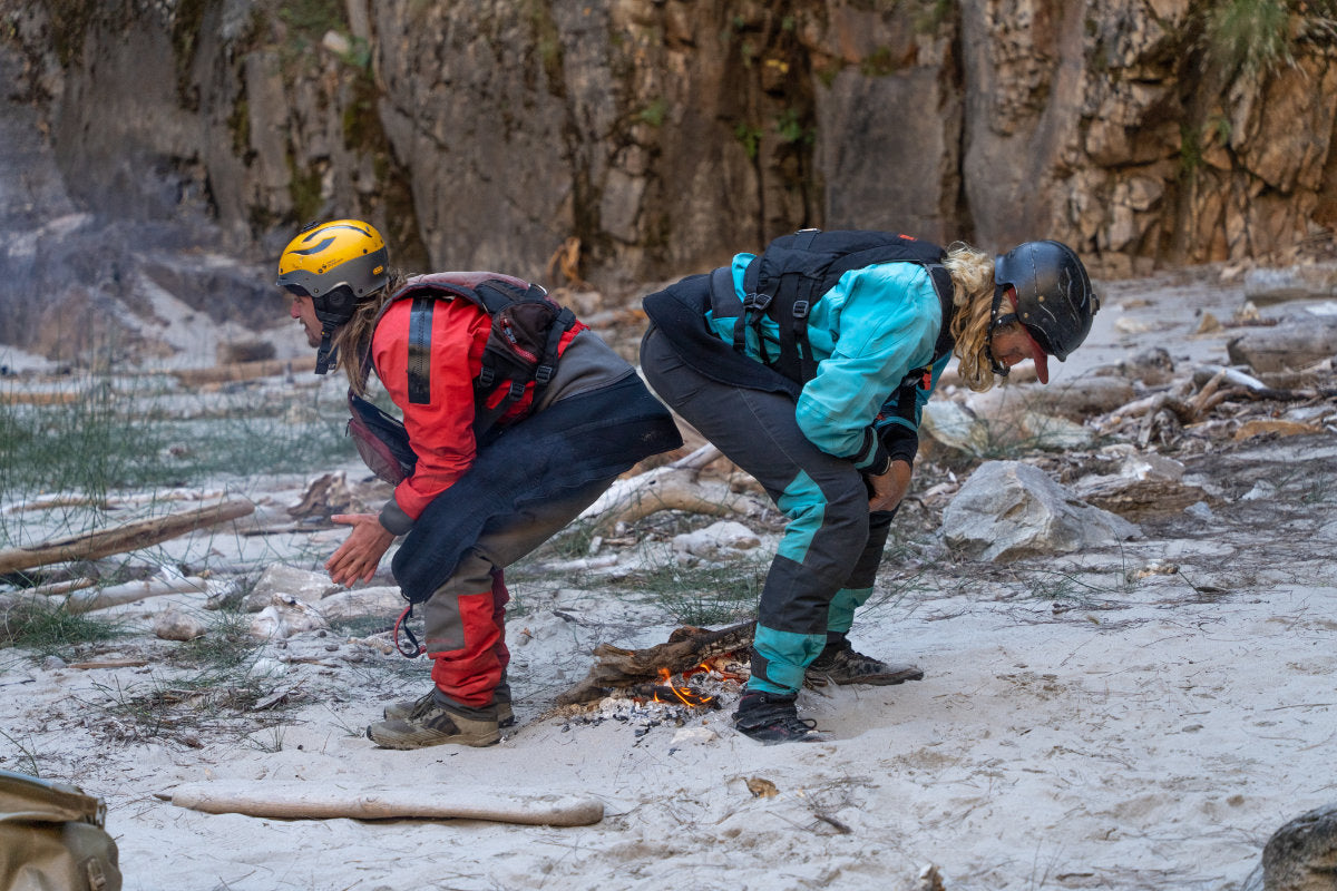 Two kayakers squatting over camp fire to warm up and dry out