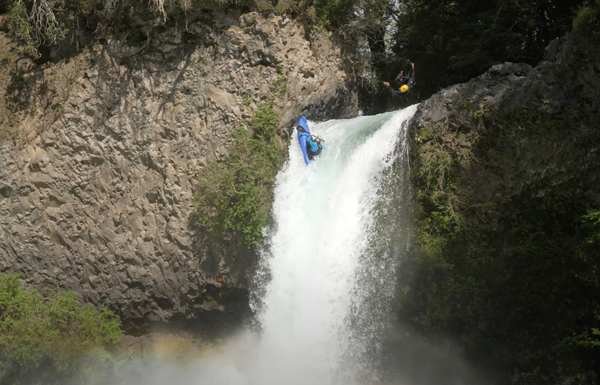 Two whitewater kayakers paddling and jumping off a waterfall.