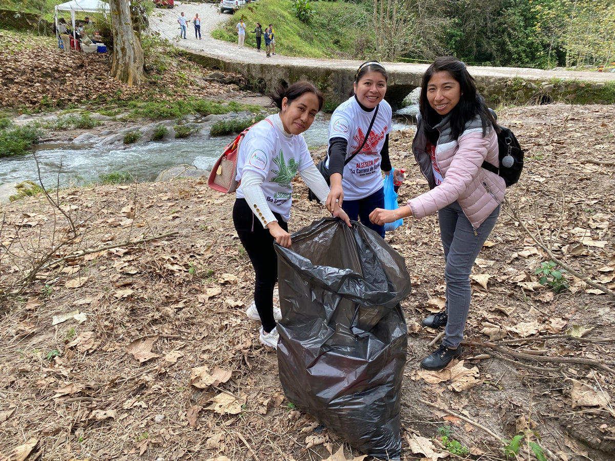 Three women cleaning up trash and debris on the river bank.