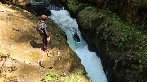 A kayaker setting safety next to a rapid as another packrafter paddles the rapid.