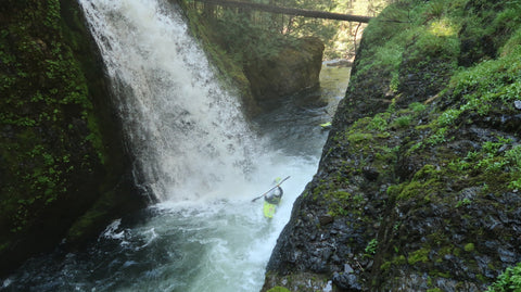 A kayaker paddling through the bottom of a waterfall.