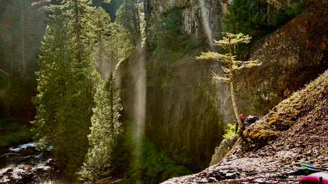 Two Kayakers tying off a climbing anchor to rappel down a cliff in order to portage a waterfall.