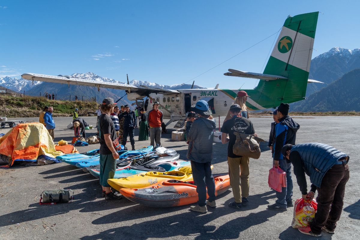 People standing near a small plane waiting to load whitewater kayaks into cargo area