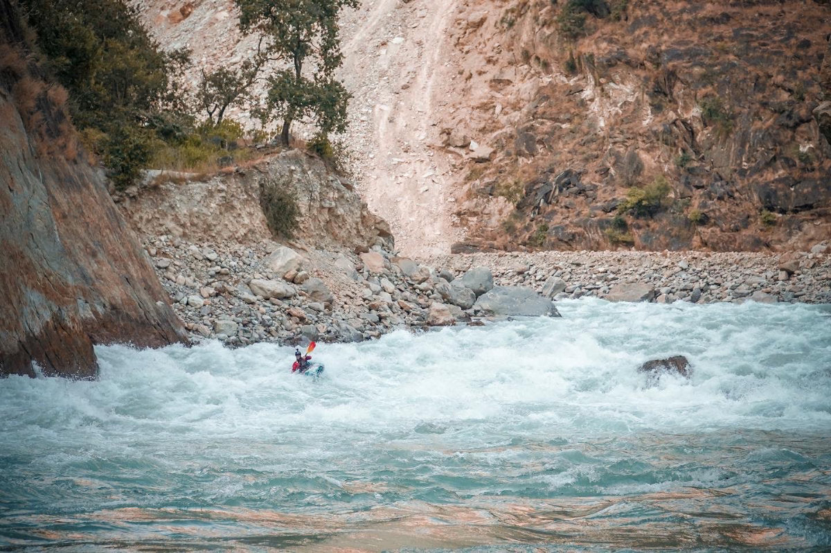 Kayaker paddling high volume whitewater river with cliff walls on both sides