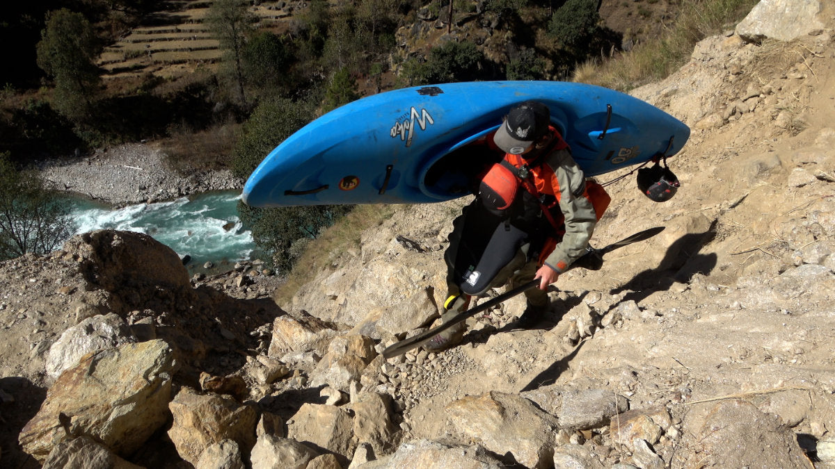 Kayaker carrying kayak while portaging a rapid high above the river