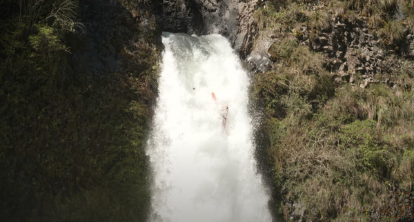 Whitewater kayaker paddles a waterfall while a rock breaks off the lip.