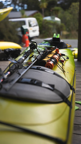 A Sea kayak geared up with fishing pole and supplies for a paddling trip.