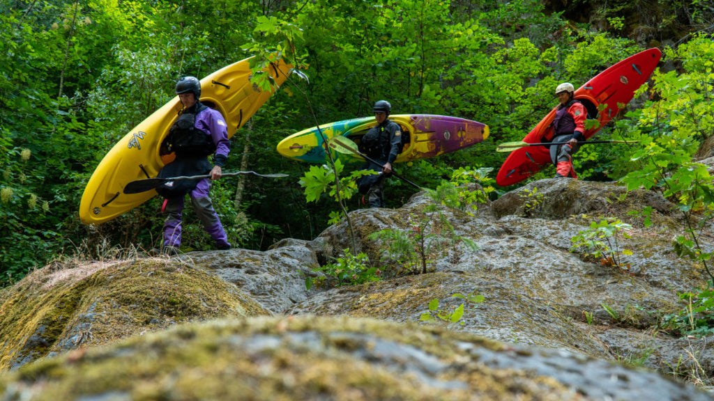 3 kayakers walking in dry creek bed while carrying whitewater kayaks