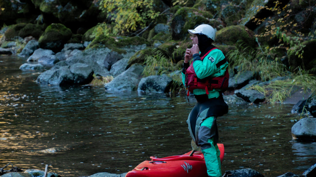 Whitewater Kayaker wearing a drysuit gears up beside a river