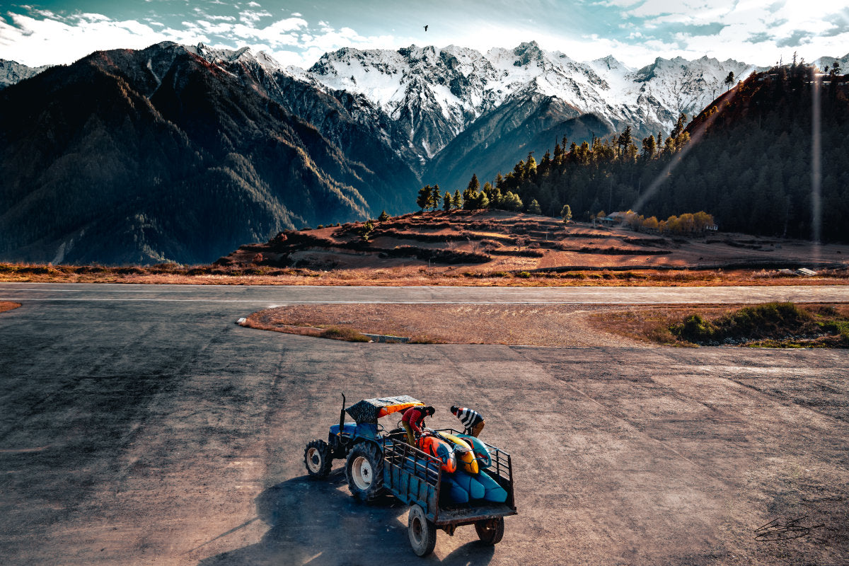 Tractor pulling trailer full of whitewater kayaks with mountains in the background