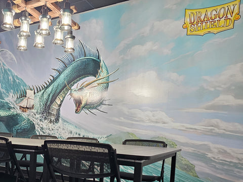 A peek at the Halcyon Games private room with a dragon image on the wall, a wooden light fixture, and a table with chairs around it.