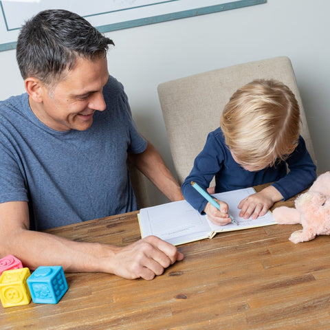 dark haired man writing with young son in a family journal