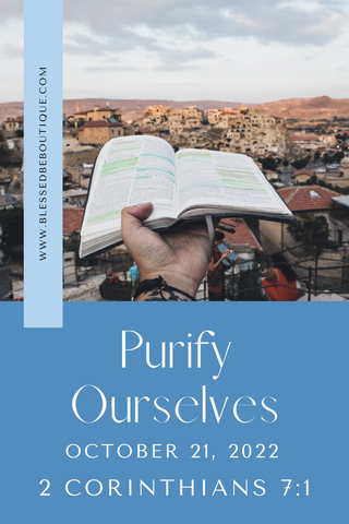 Image of a hand holding an open Bible over a cityscape with the words "purify ourselves, October 21, 2022, 2 Corinthians 7:1"