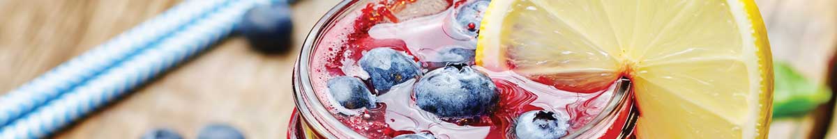 Glass of blueberry lemonade with fresh blueberries and ice and a twist of lemon on glass edge.