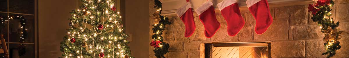 A festive holiday tree decorated with ornaments and lights and stockings hung over a fireplace.