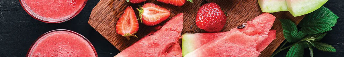 Strawberries and watermelon on a cutting board with green leaf sprigs.