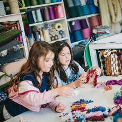 2 girls sitting next to each other while weaving in a workshop for the Textile Arts Club at The Oxford Weaving Studio