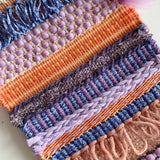 Detail image of handwoven fabric featuring colours, patterns and textures in purples and oranges