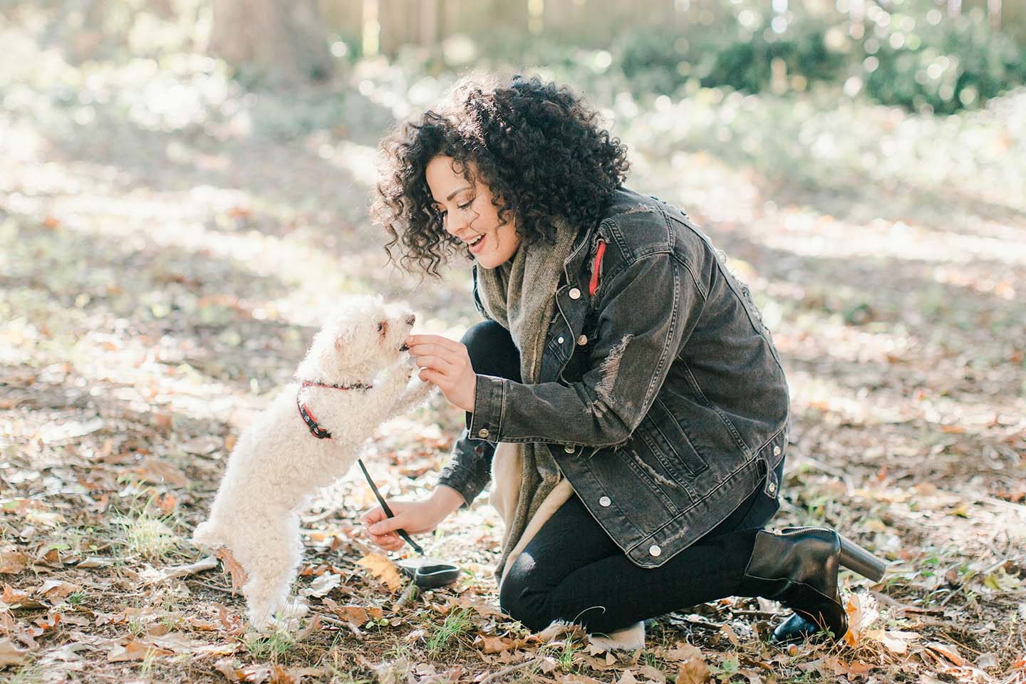 A woman feeding something to a small dog on a leash.