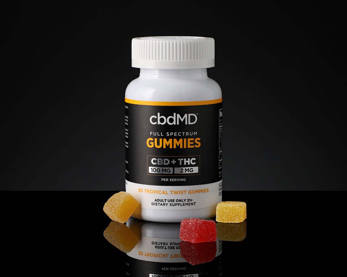 a jar of cbdMD Full Spectrum CBD Gummies with several red and yellow gummies on a black background