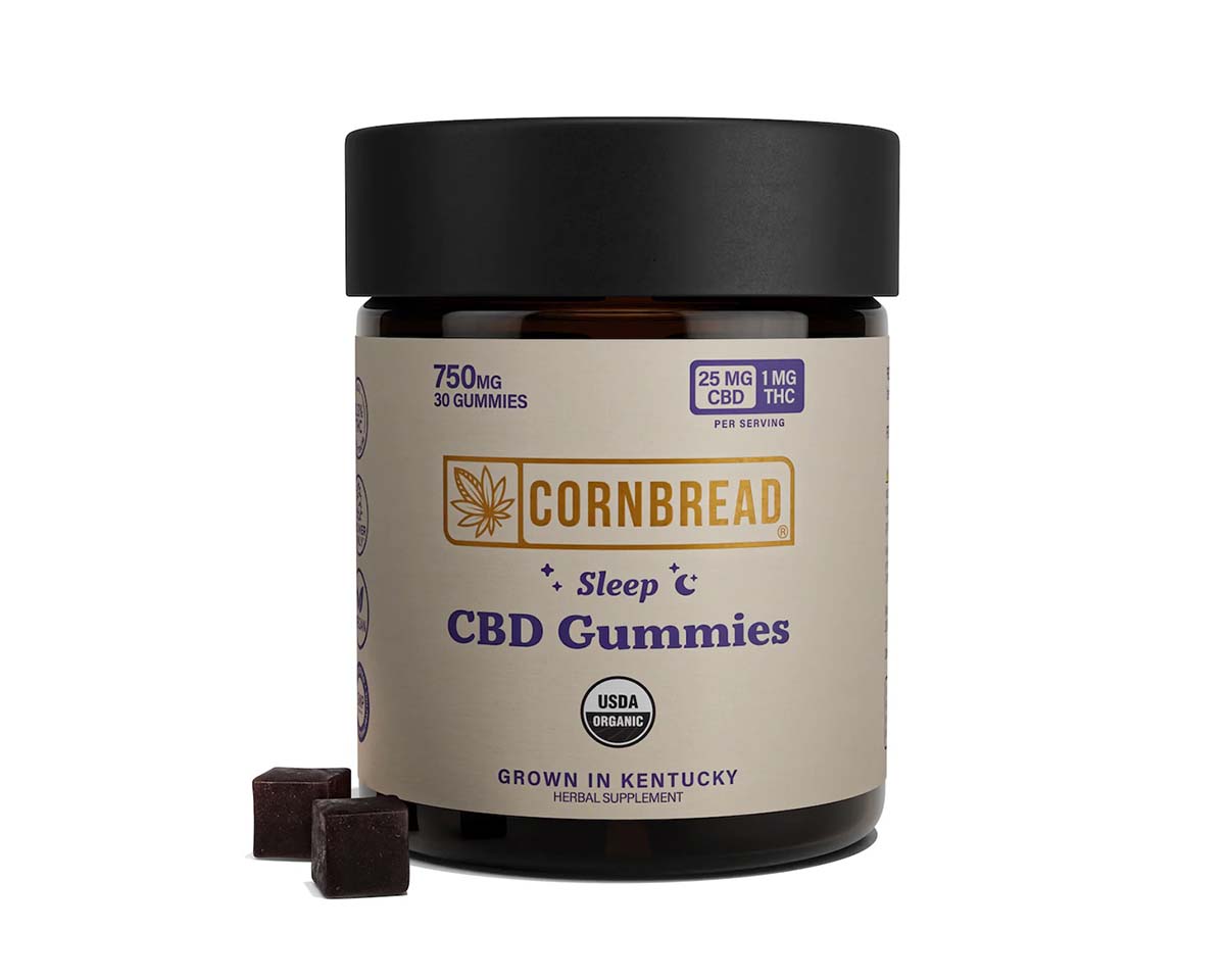 Two dark-colored CBD gummies next to a jar with a tan label